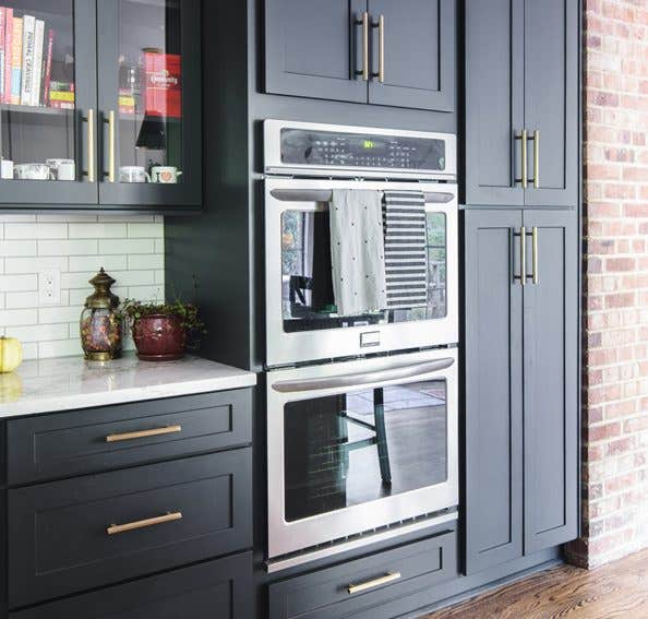 Kitchen using CliqStudios Shaker cabinets in black with white countertops, stainless steel double ovens, and exposed brick walls.