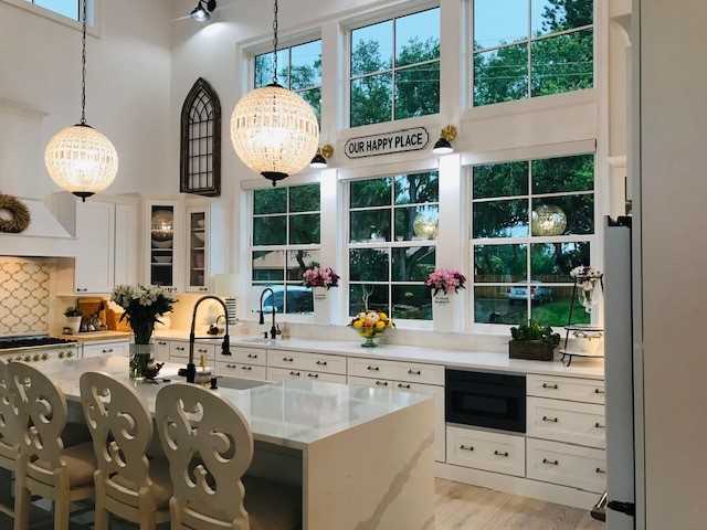 White shaker cabinet kitchen with large mullion windows over sink, custom wood hood, and large island with waterfall quartz countertop