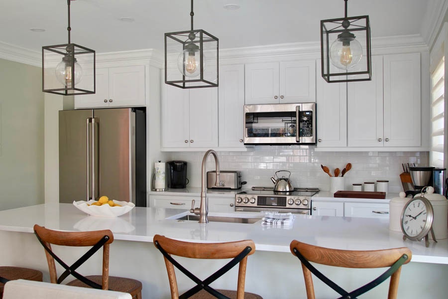 Kitchen with white shaker cabinets, black metal fixtures, stainless appliances and wood chairs on peninsula