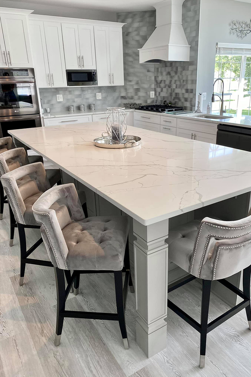 L-shaped open shaker white kitchen with decorative hood and large island with furniture legs