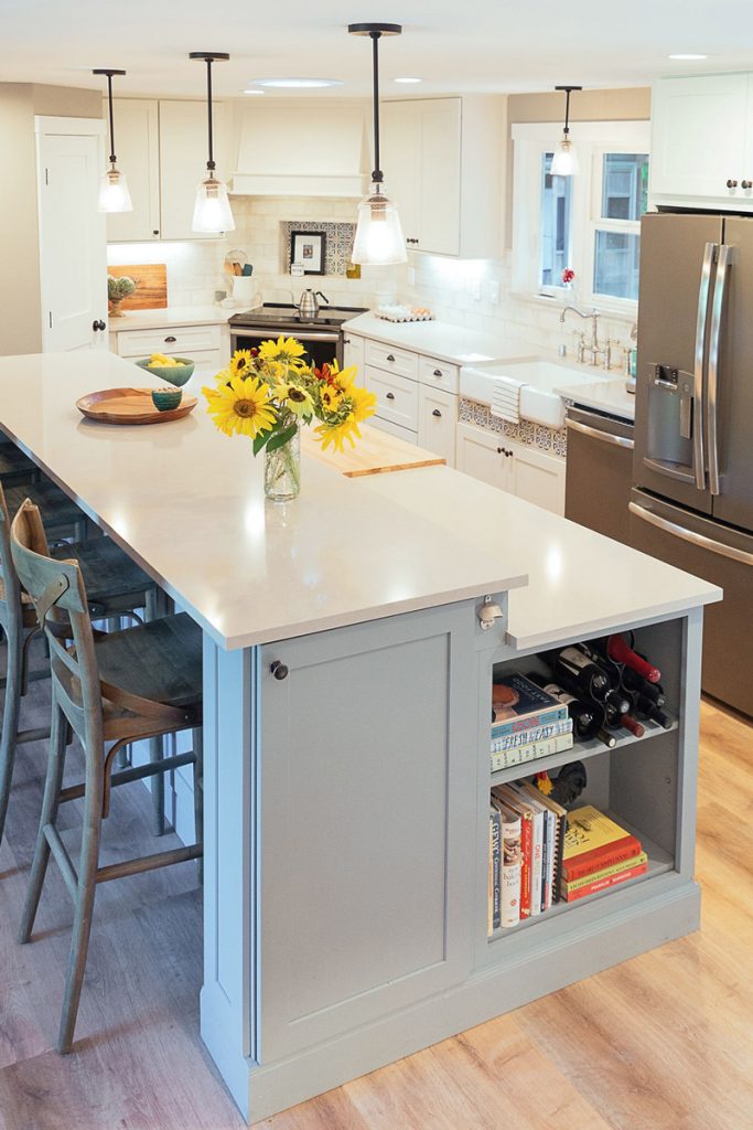 White kitchen with large two-tier blue island, stainless appliances and corner range