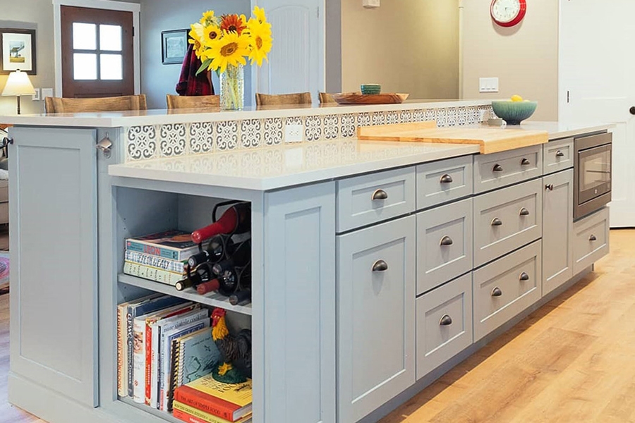 Large blue-gray color two-tier island with white countertops and blue tile backsplash and farmhouse hardware cup pulls