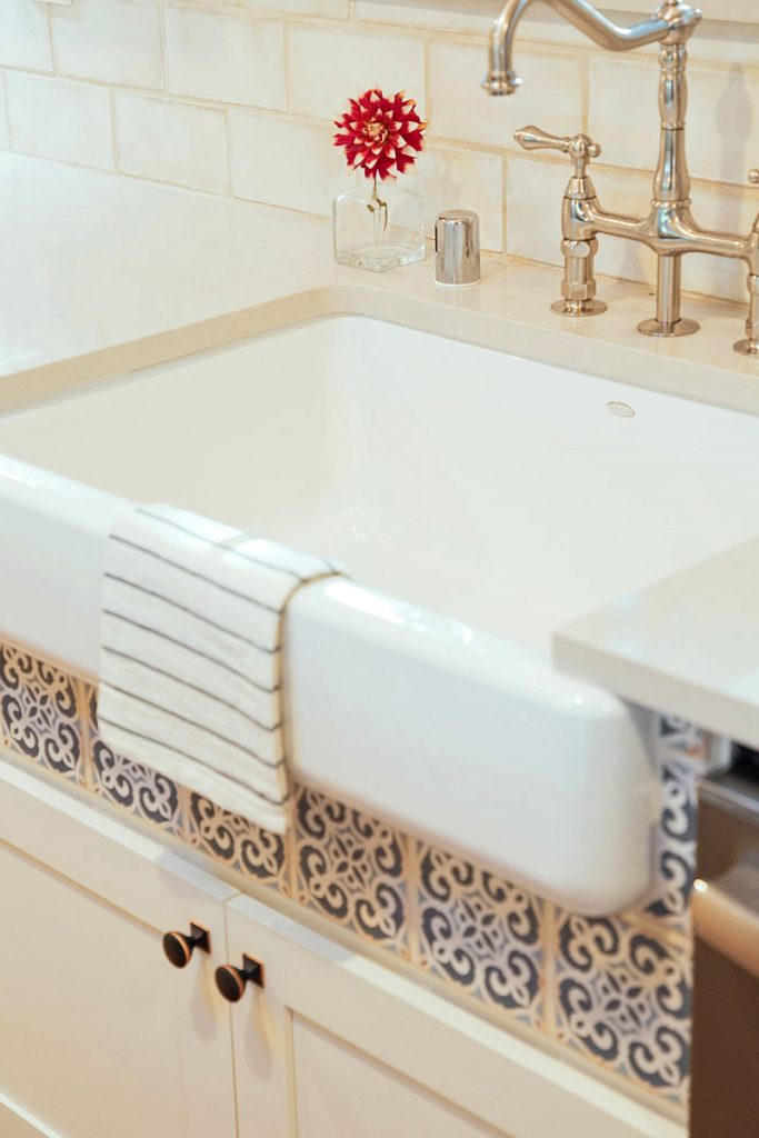 White apron sink with blue tile detail below the front skirt