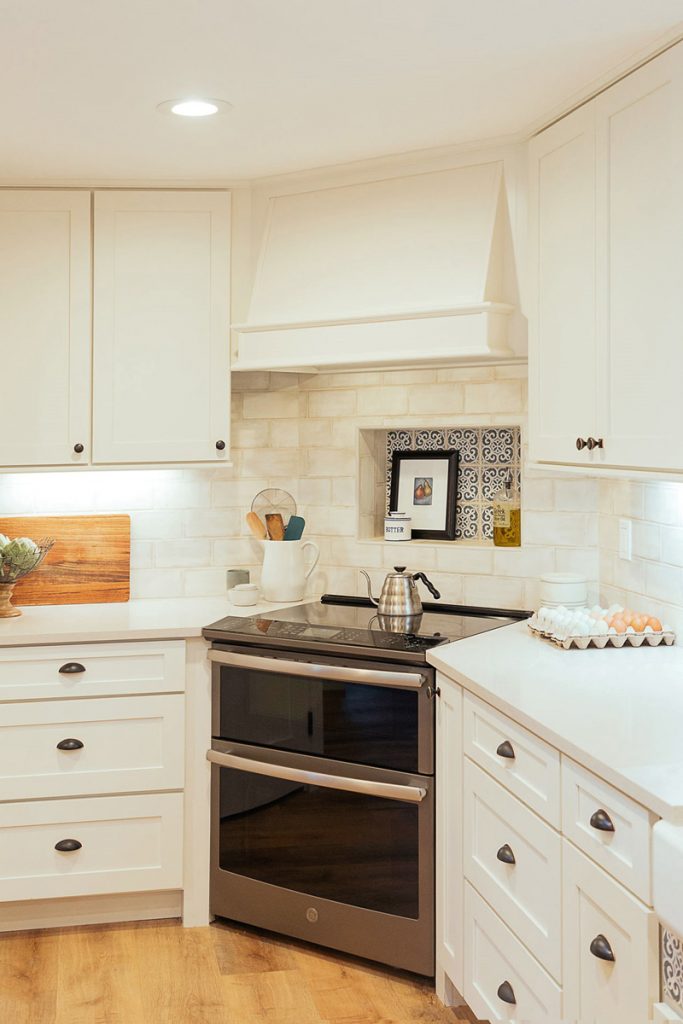 Stainless steel range in the corner of a kitchen with white cabinets and range hood