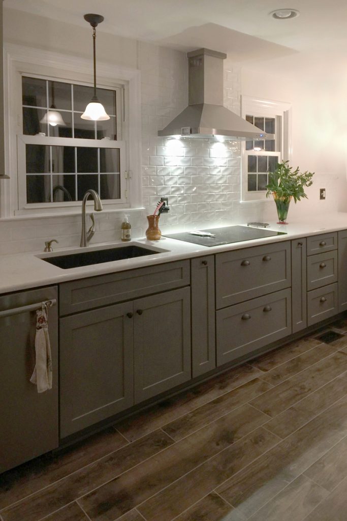 Cooktop with stainless hood, white backsplash and gray storage cabinets below