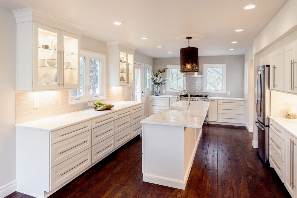 White shaker U-shaped kitchen design with long island in the center, glass wall cabinets, brushed nickel bar pulls, and white stone countertops