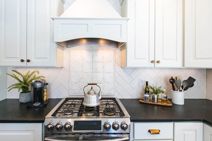 A kitchen stove top and wooden range hood with a white subway tile backsplash