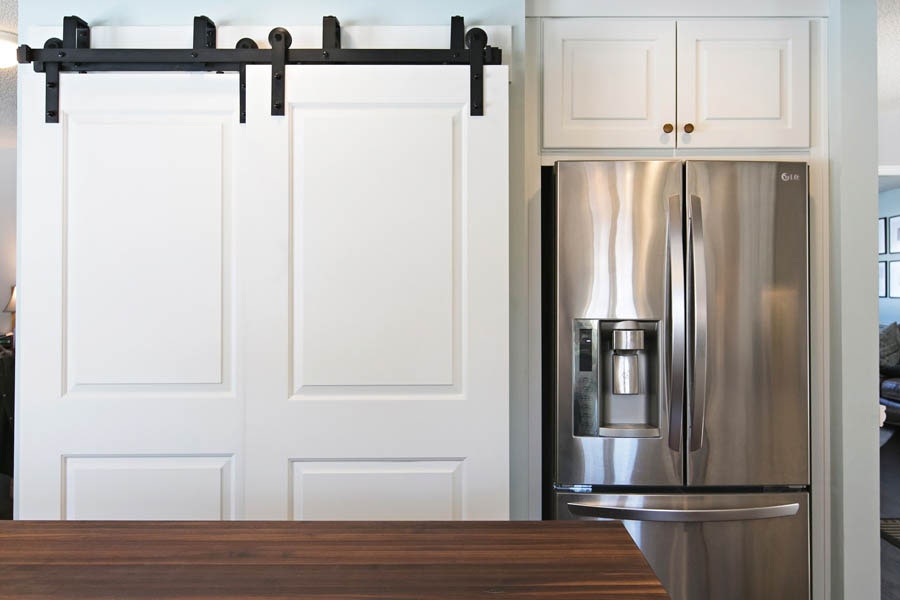 A white sliding farm door next to a stainless steel fridge.