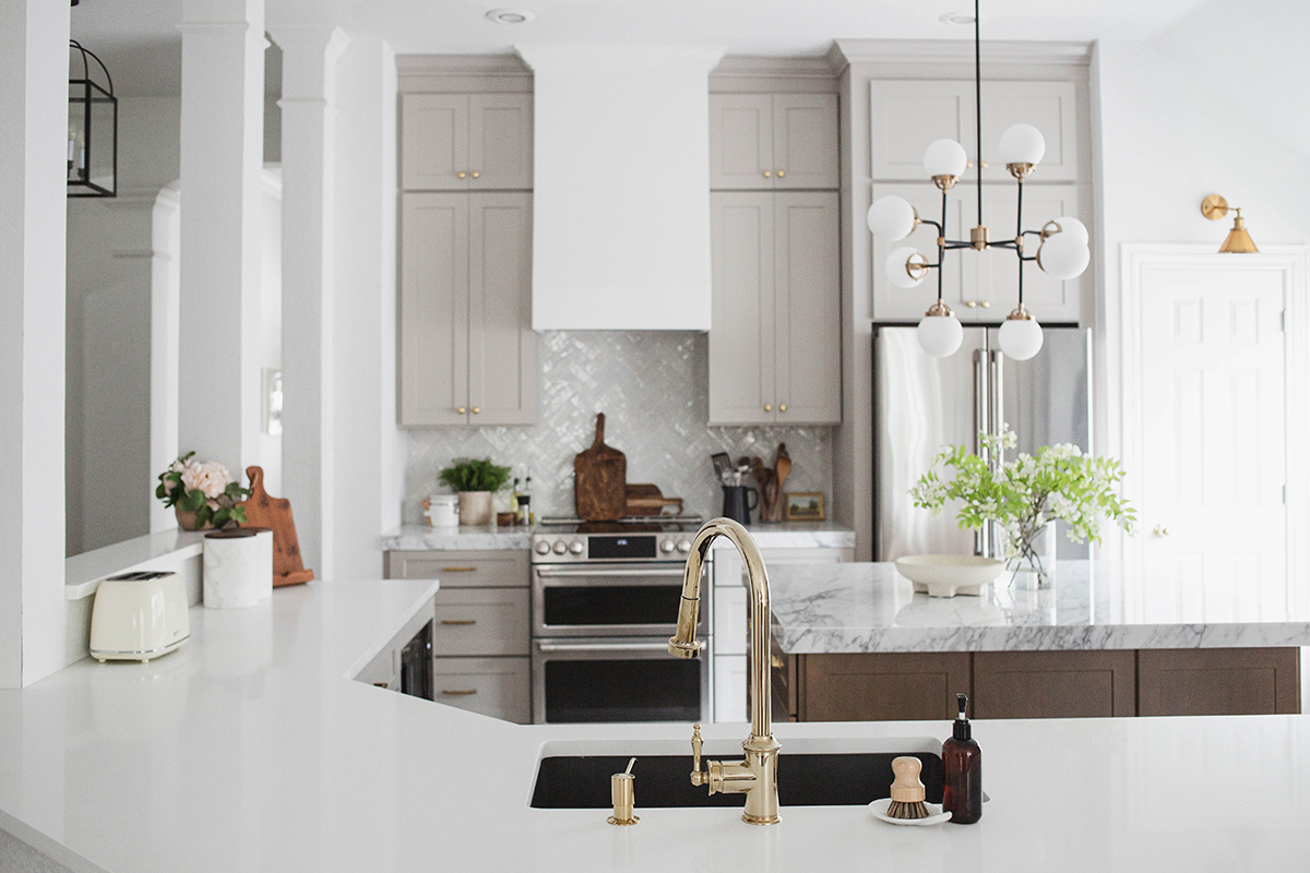 CliqStudios project: Light gray shaker kitchen cabinets and chestnut stained island with marble countertops and white, gold, and black accents