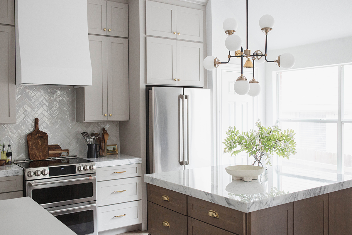 CliqStudios project: Light gray shaker kitchen cabinets and chestnut stained island with marble countertops and white, gold, and black accents