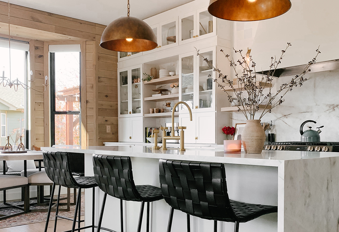 White shaker kitchen with stacked furniture buffet cabinets with glass, brass hardware and pendant lights, and waterfall island countertop