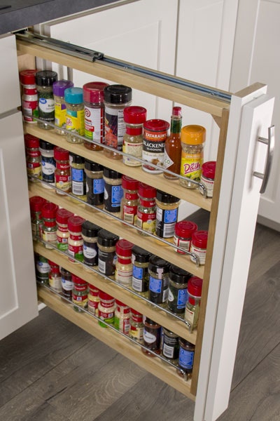 Pull-out storage cabinet with three shelves storing spices and seasonings.