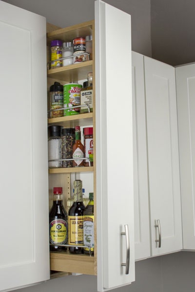 Pull-out storage cabinet with three shelves storing spices and other small assorted jars.