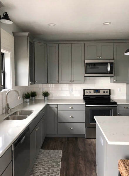 Gray Shaker cabinets surrounded by white countertops and backsplash with undermount sink and stainless appliances.