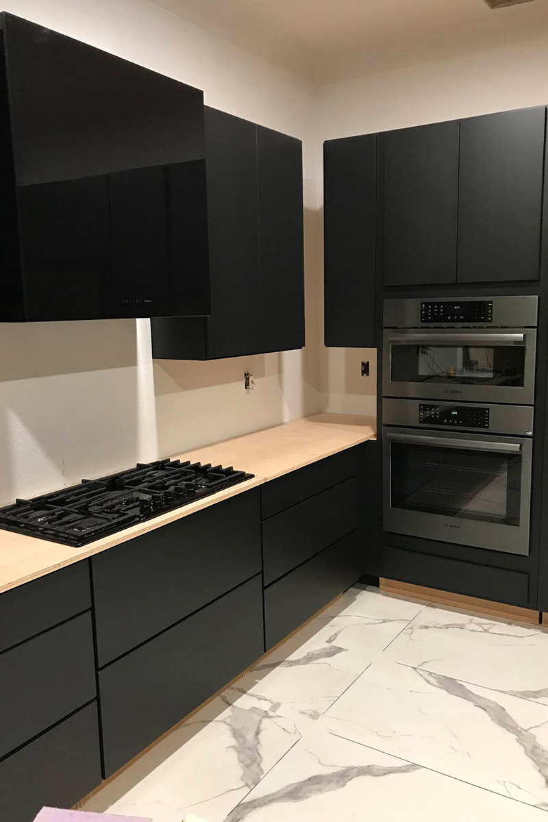 Black painted kitchen cabinets in slab door, dark appliances, and white marble tiled floors