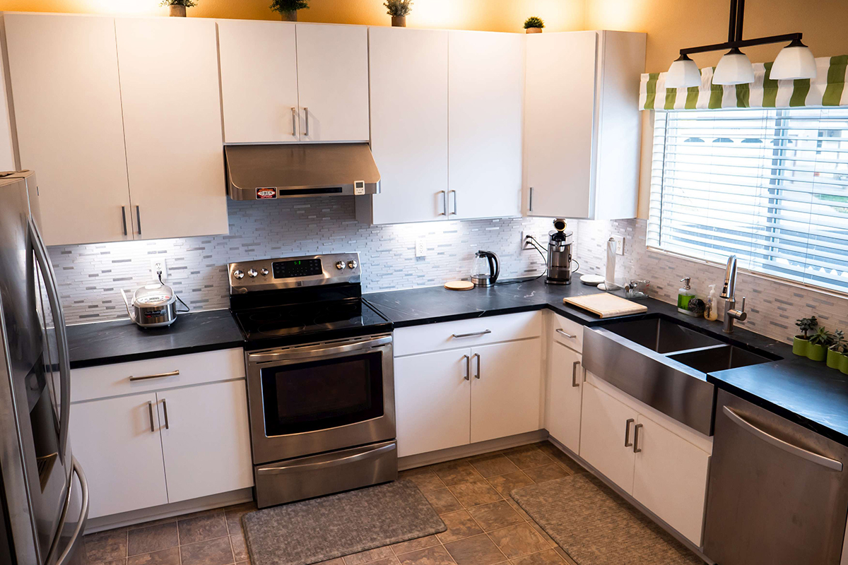 CliqStudios project: Slab white kitchen cabinets with stainless steel appliances and stainless steel apron sink