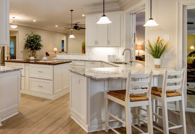 kitchen with white shaker cabinets has center island with butcher block countertop, peninsula with rattan bar stools, potted plants on counters and hardwood floors