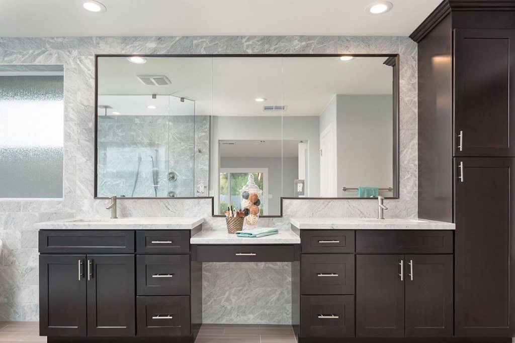 Dark espresso shaker vanity cabinets in master bath with two sinks separated by a makeup desk and tall linen closet on the right side