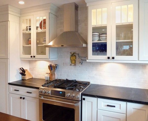 kitchen with glass door cabinets on either side of professional stainless range hood with under-cabinet lights, white shaker cabinets and black granite countertops