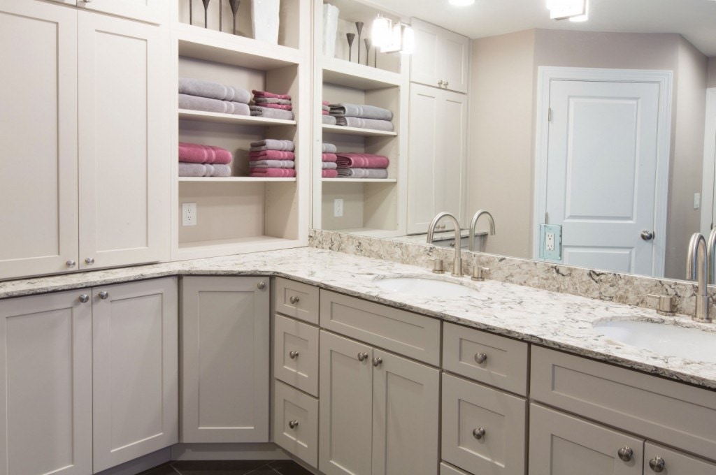 L-shaped white shaker vanity cabinets in a master bath with two sinks, open shelves and pantry storage.