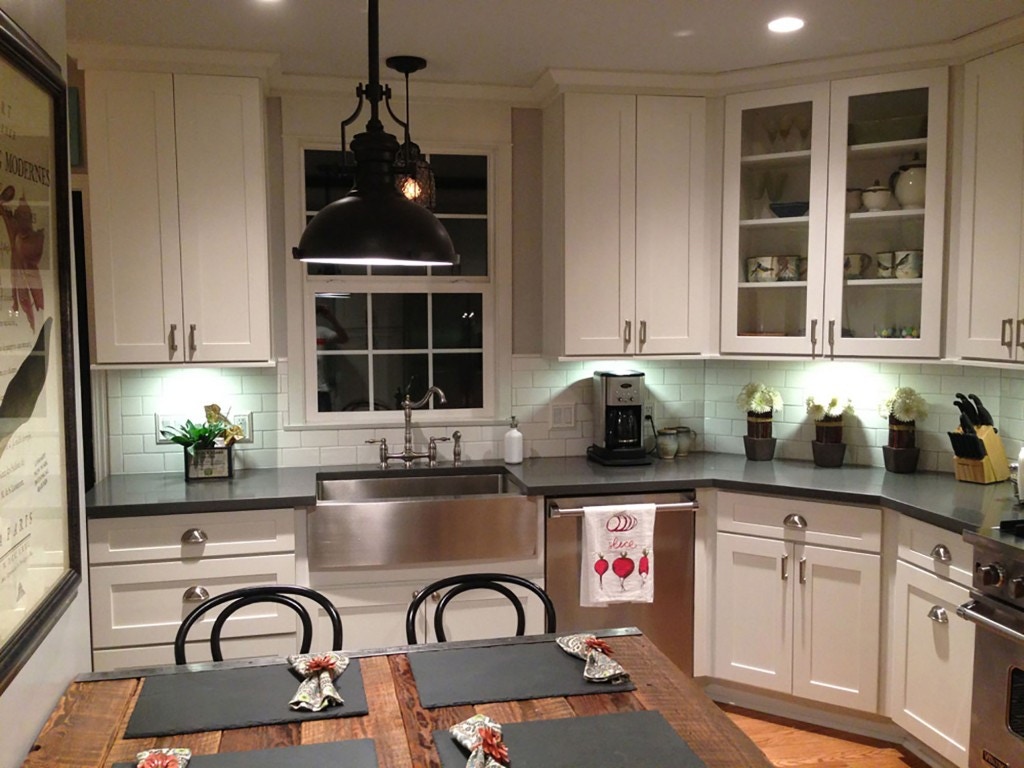 kitchen renovation features white Shaker cabinets, stainless apron sink, black quartz countertops and glass-door cabinets on angled wall