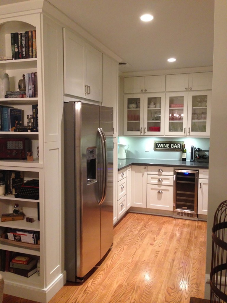 California kitchen features glass door cabinets above beverage center, built-in refrigerator flanked by open bookshelves and medium tone oak floors