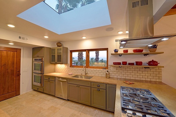 kitchen with moss green shaker cabinets, large square skylight, open shelves with potter and peninsula with pro cooktop and stainless hood