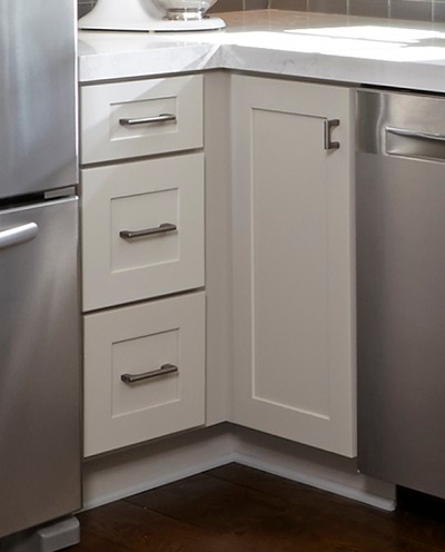 closeup of white shaker cabinets in corner showing spacer by the drawer base and door-only cabinet used to allow cabinets to open freely past projecting bar pulls