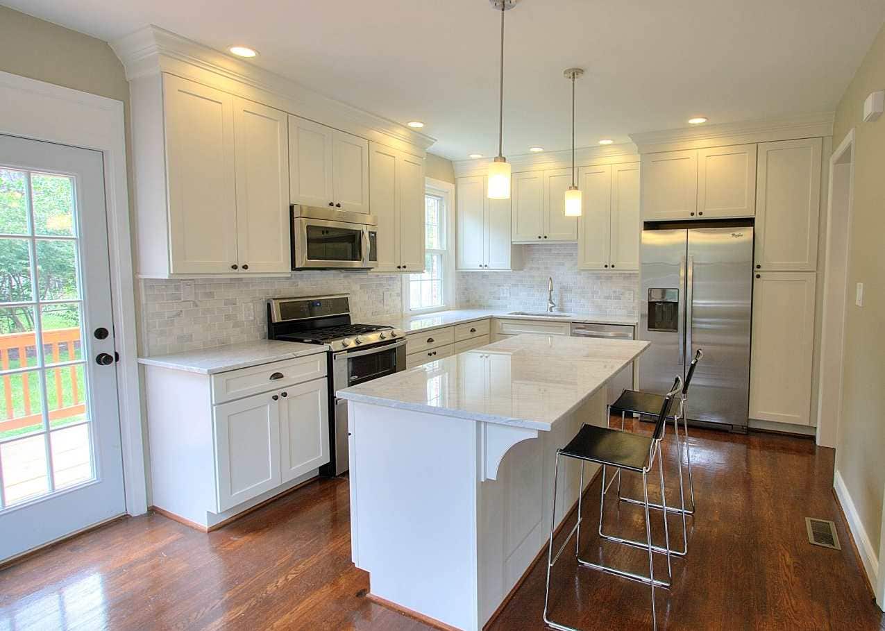 Kitchen has white Shaker cabinets, mullion window and french doors, rich oak hardwood floors and a center island facing the french doors