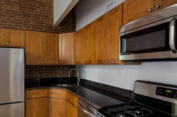 new york apartment kitchen before renovation had red brick wall, oak cabinets, black countertops and a corner sink