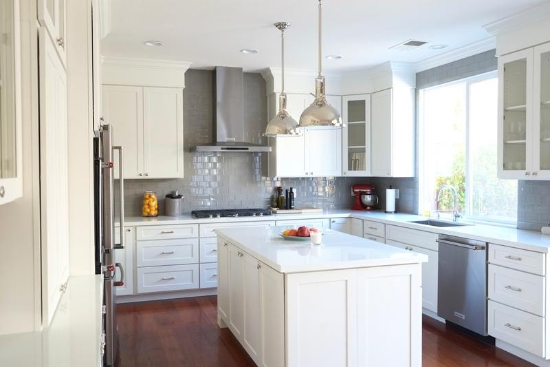 Industrial luxe kitchen features white shaker cabinets, white glass subway tile backsplash, stainless island pendants, glass door cabinets and built in buffet