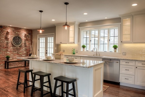 shaker white cabinets in small open kitchen with wide-plank oak floors, brick wall and mullion windows and glass cabinets lit from inside