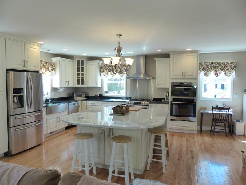 open kitchen viewed from family room has large island with seating on two sides, white traditional cabinets, oversized stainless apron front sink and ornate chandelier over island