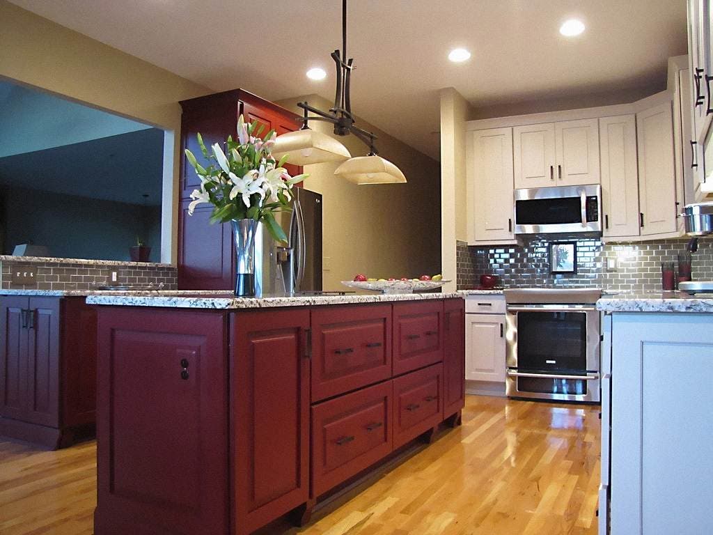 Two-tone kitchen with red center island and white perimeter cabinets in a raised panel cabinet style with gray granite countertops and hardwood flooring