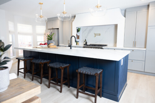 Large one-wall kitchen design with tall light gray shaker kitchen cabinets and gold cabinet hardware with a long dark blue kitchen island and white quartz countertops