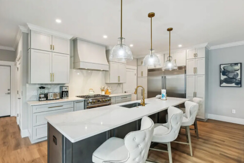 Large light gray shaker kitchen with matching wood hood, stacked cabinets with crown molding and a dark brown stained kitchen island