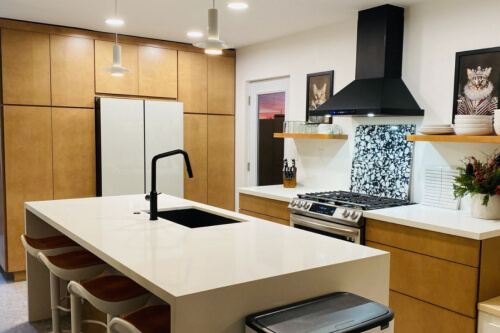 Mid-century modern kitchen design with light brown slab kitchen cabinets and a cream-colored waterfall quartz countertop