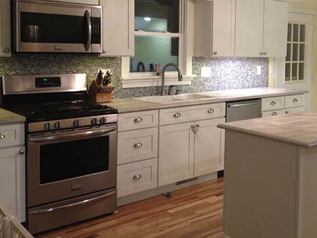 Kawanee Illinois kitchen with white Shaker cabinets, stainless gas range, microwave and dishwasher, original oak flooring, custom countertops and brilliant small tiles in the backsplash