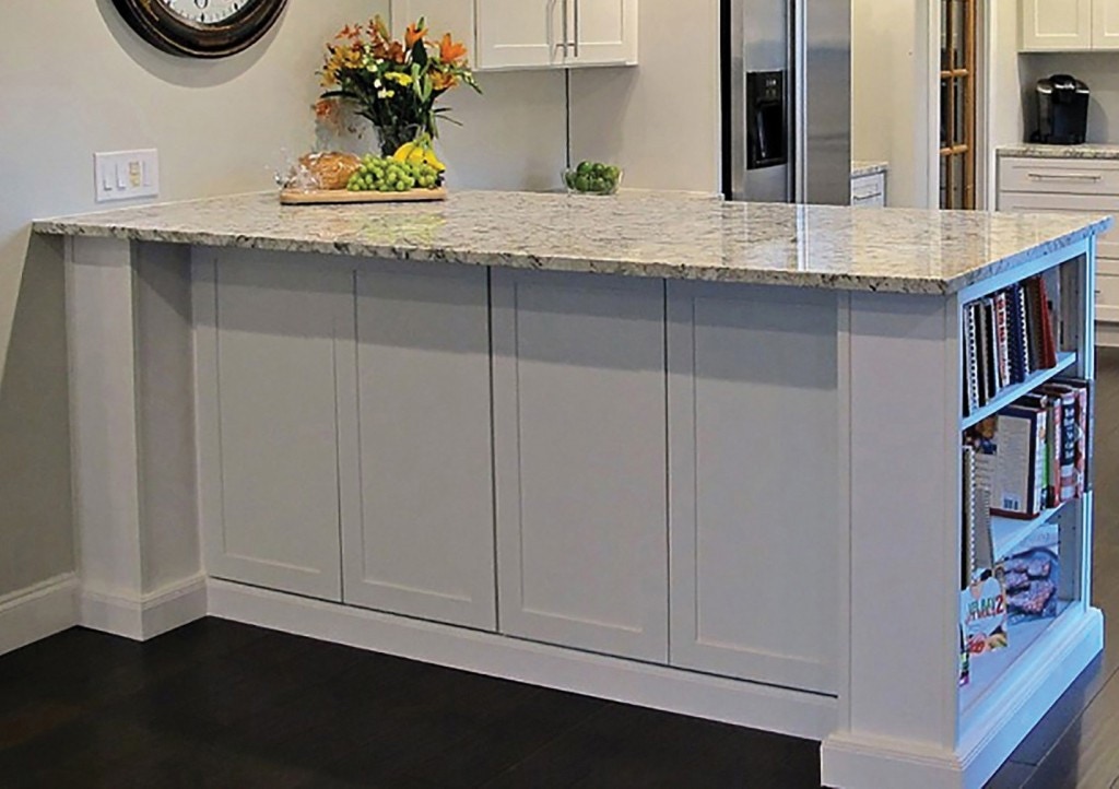 Kitchen peninsula in white cabinets with bookcase end, decorative door panels on back and ogee molding in toe kick