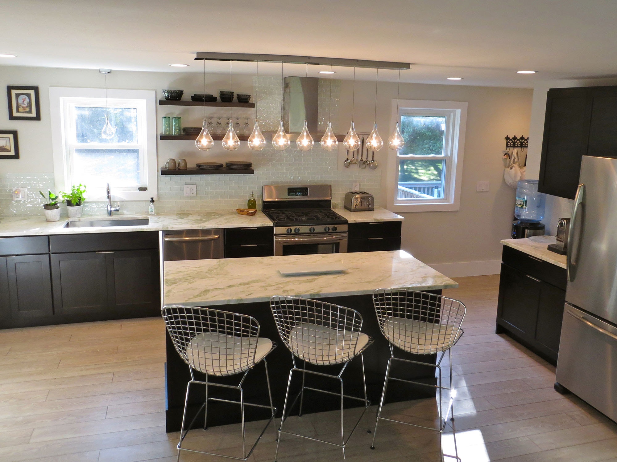 kitchen with black cabinets, white subway tile backsplash, open shelves, bare bulb light pendants and woven wire bar stools