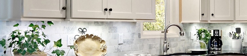 Closeup of light rail skirt trim on painted cream shaker cabinets with gray marble backsplash and ivy on counter