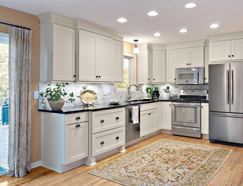 L-shaped white shaker kitchen cabinets with decorative crown molding and a drawer base bump-out with decorative feet