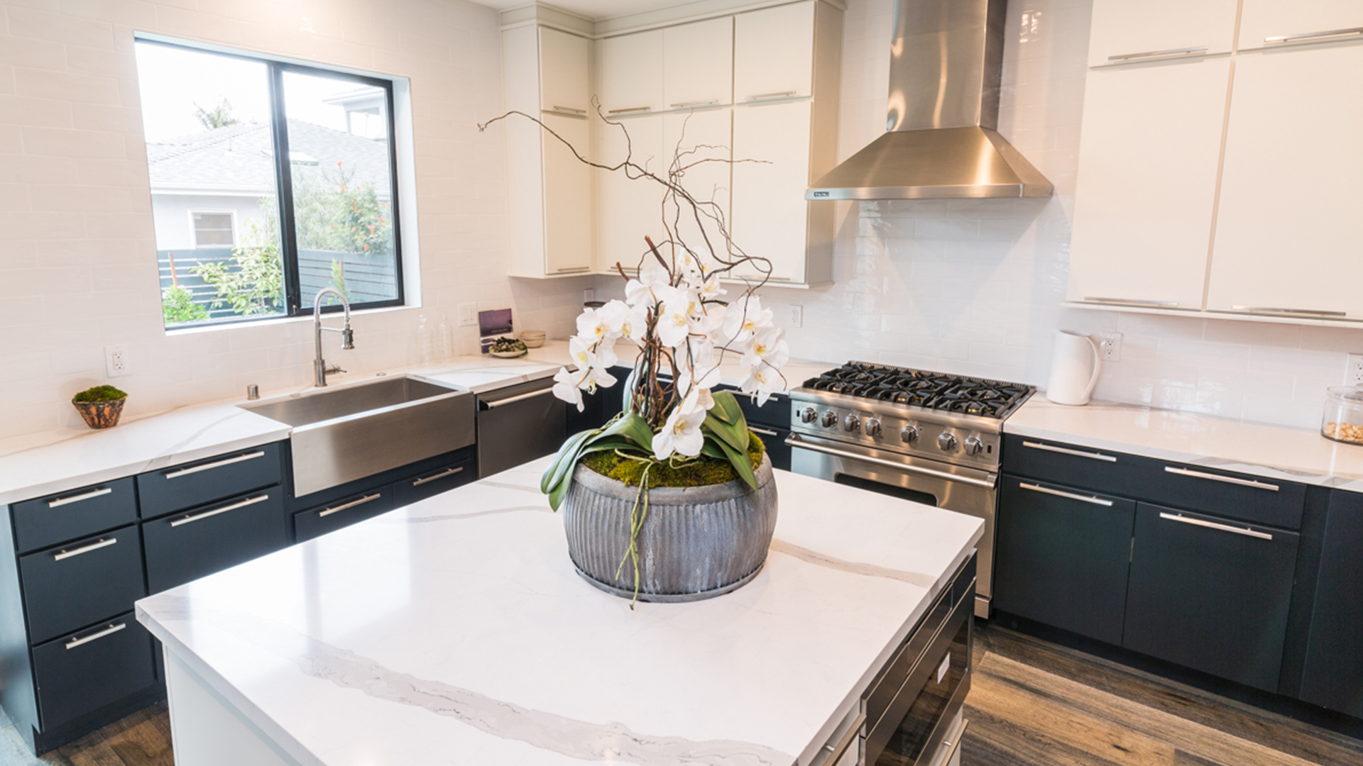 L-shaped slab door style kitchen and island with white wall cabinets, black base, and island cabinets, with nickel bar pulls 