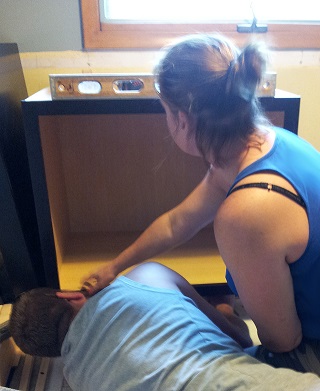 Designer Tessa and husband Jake work together, leveling a base cabinet in their kitchen