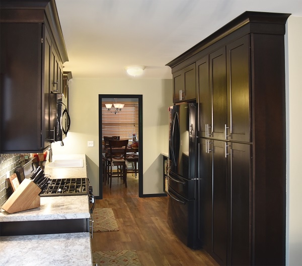 galley kitchen has wood-look vinyl tile floor, ebony cabinets in a shaker style, glass backsplash and granite-look laminate countertop