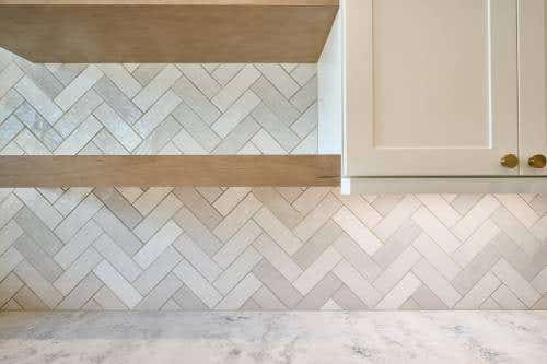  White shaker cabinets with a light cream herringbone tile backsplash and light wood floating shelves 