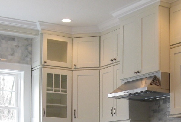 picture of white wall cabinets including glass mullion door, angle cabinet, custom wood range hood and decorative crown molding