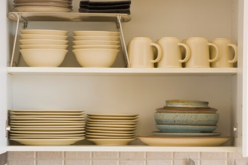 White open kitchen cabinet with organized plates, bowls and cups inside