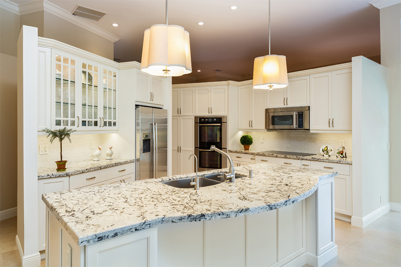 Traditional large white shaker kitchen design with baseboard and crown molding, mullion glass doors, stainless steel appliances, and white and brown speckled granite countertops.