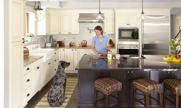 woman cooking at center island smiles at large dog sitting nearby in kitchen with cream raised panel cabinets on perimeter and dark furniture look island